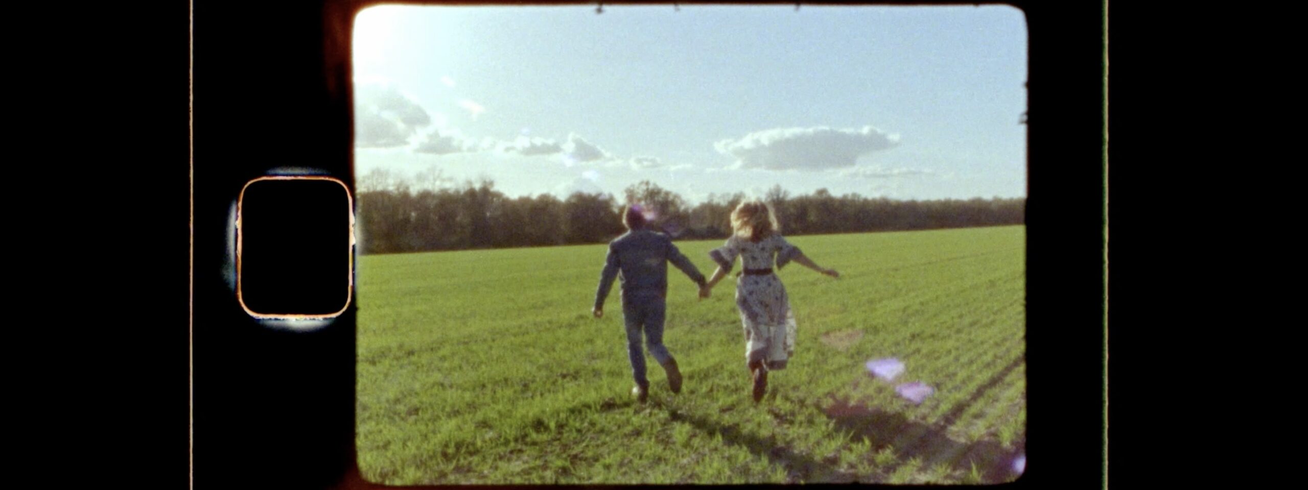 A super8 still of an older couple holding hands an running through a field