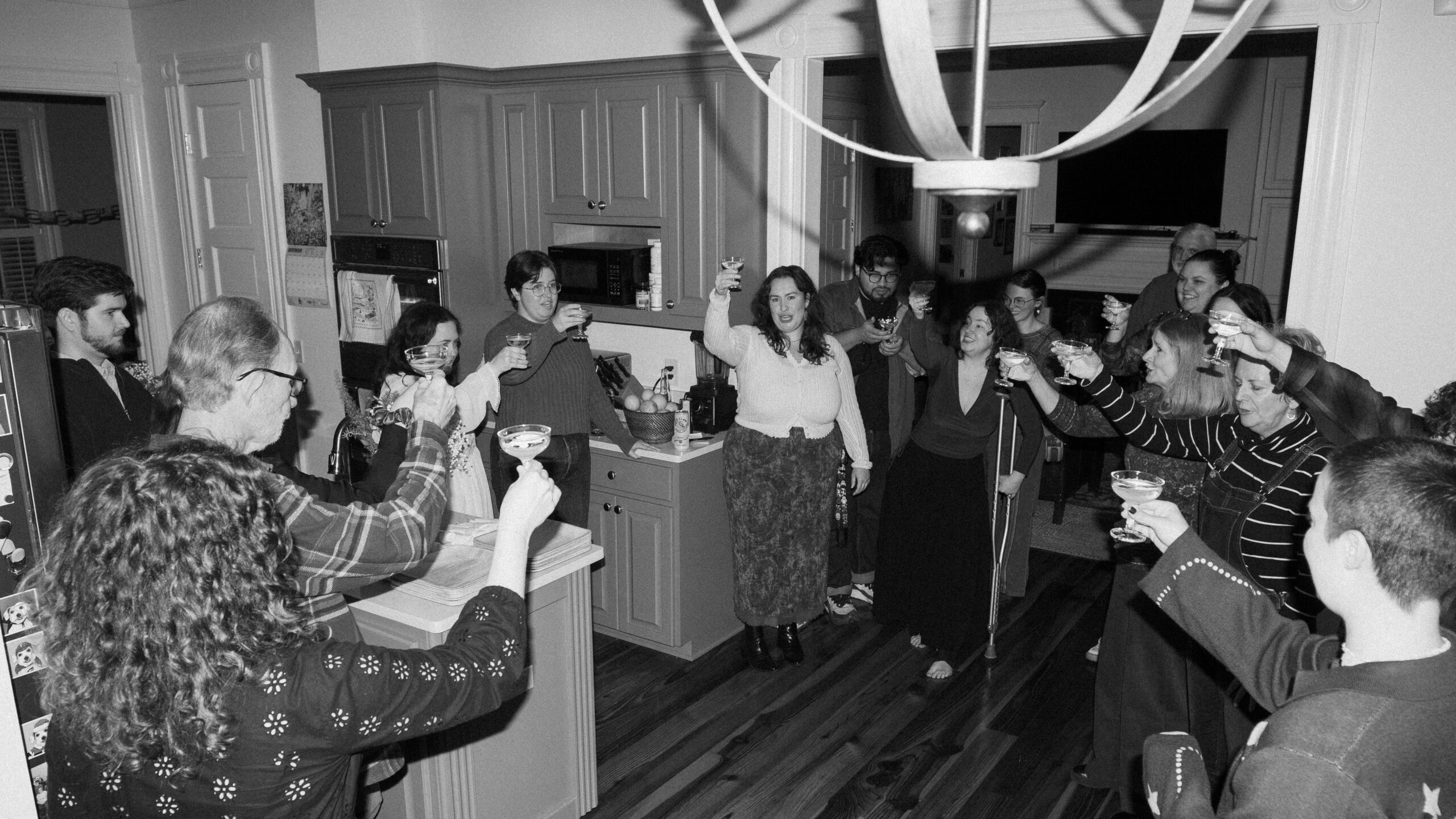 A black and white photo of a crowd giving a toast in kitchen