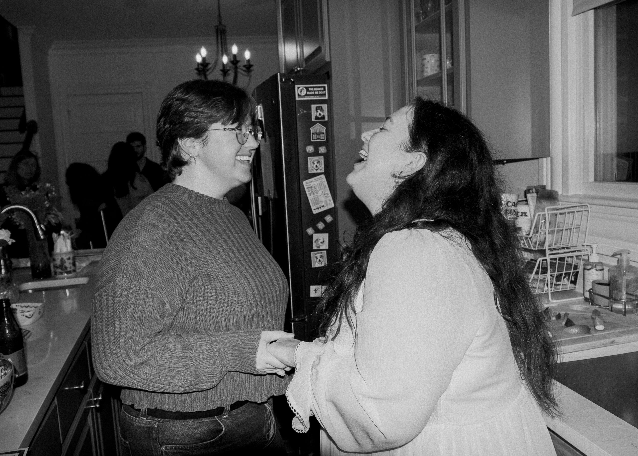 A queer couple holds hands and  laughs during their engagement party