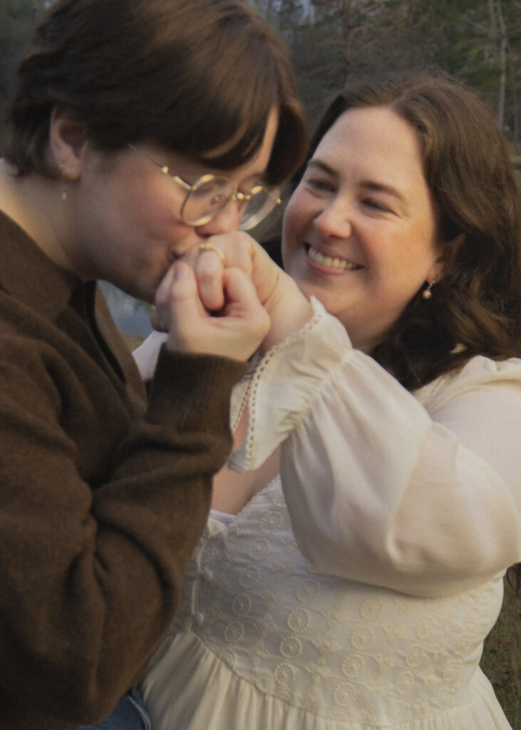 A romantic film photo of a queer couple, one person kisses the others hand and an engagement ring is clearly visible