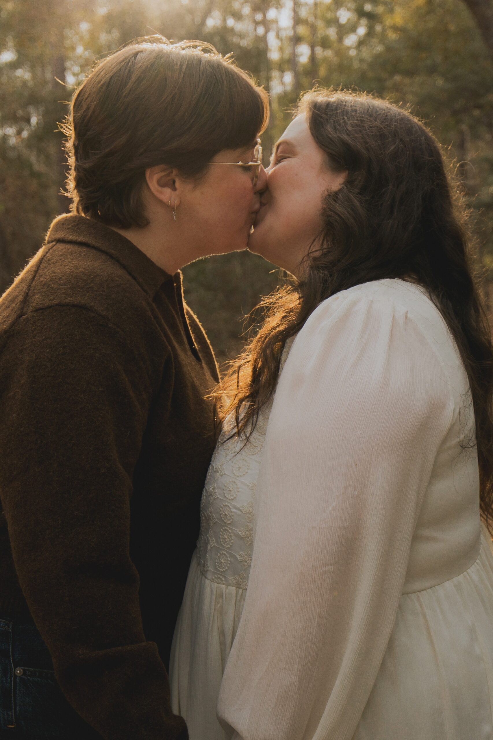 A cinematic photo of a lesbian couple kissing in golden, hazy light.