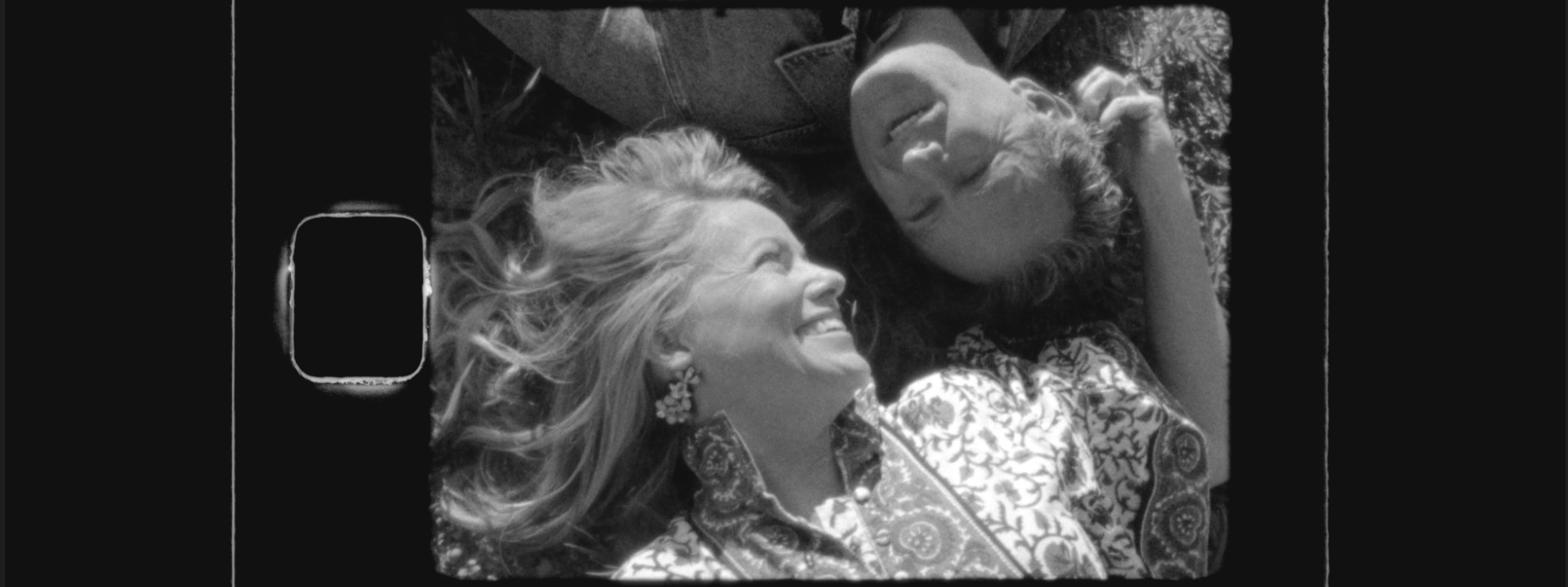 A still from Super 8 film, a couple looks at each other while laying down in a rye grass field in Moultrie GA