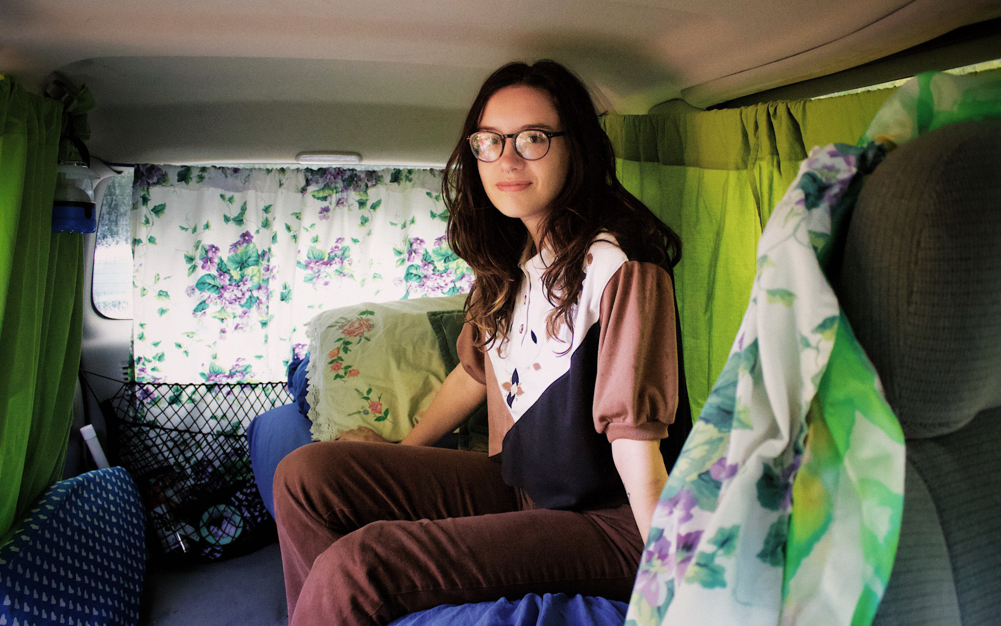 Queer travel photo, a nonbinary person sitting in their travel van with shot light and layered fabrics in Athens Georgia
