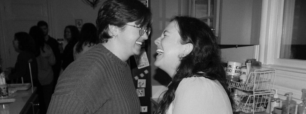A lgbtq couple laughs at their engagement party, with family in the background