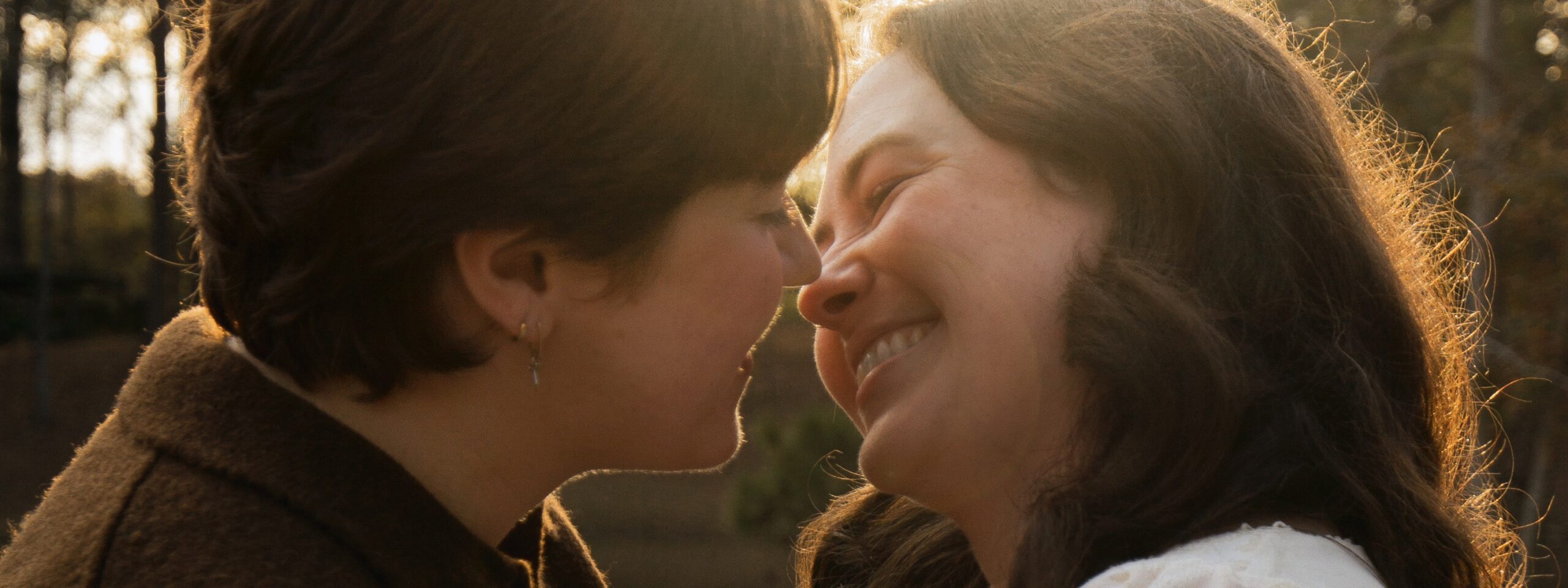 A queer couple smiling and kissing in golden light